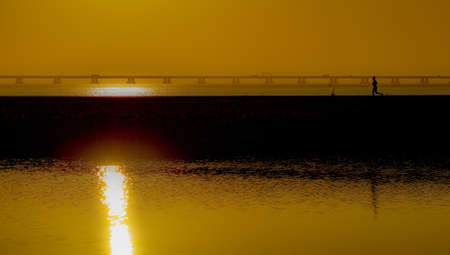 A beautiful shot of a person running on a dock over the sea with the reflection of the sunset