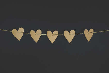 A closeup shot of heart-shaped cut-outs on a string with a black background