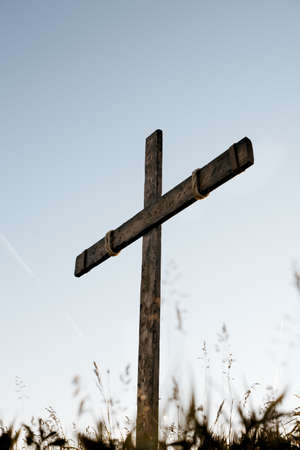 A low angle vertical shot of a handmade wooden cross with a blue sky in the backgroundの写真素材