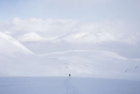 A horizontal shot of a male standing in a snowy area with a lot of high mountains covered with snowの写真素材