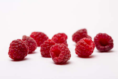 A closeup shot of fresh raspberries spread on a white background - perfect for a food blog
