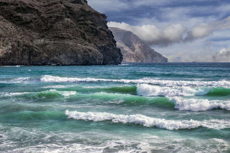 A landscape shot of the sea waves near rocks under the blue sky