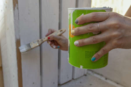 A selective focus shot of a women hand holding a metal paint can and painting a fenceの写真素材