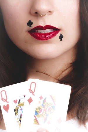 A vertical shot of a female with clubs and spades face art and red lipstick holding playing cards -...