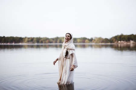 A female wearing a biblical robe and laughing while standing in the water