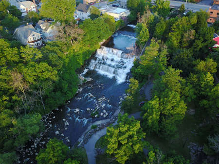 A high angle shot of a beautiful scenery with a waterfall surrounded by green trees and buildingsの写真素材