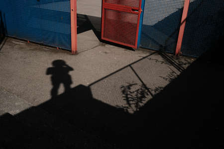 A horizontal shot of a person's shadow near a blue and red fenceの写真素材