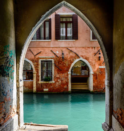 An old arch near the canal and an ancient red house with open windowsの写真素材