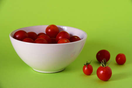 A close shot of small red tomatoes in a white bowl and on a green surfaceの写真素材