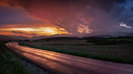 A beautiful shot of a narrow curvy road in the countryside in the middle of a field at sunset