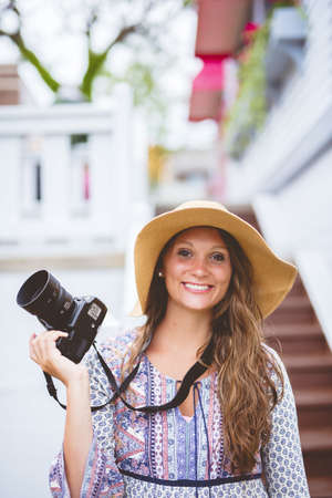 A vertical shot of a female smiling and holding a camera with a blurred backgroundの写真素材