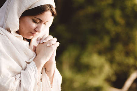 A shallow focus shot of a female wearing a biblical gown and praying while her eyes are closedの写真素材