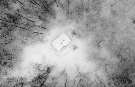 An aerial shot of a house surrounded by leafless trees in black and whiteの写真素材