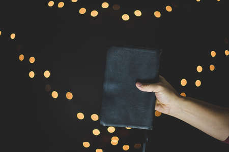 A closeup shot of a person holding the bible with blurred lights in the backgroundの写真素材
