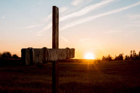 A closeup shot of a handmade wooden cross in a grassy field with the sun shining in the backgroundの写真素材