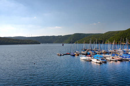 A horizontal shot of a lot of boats in the sea surrounded by beautiful green mountainsの写真素材