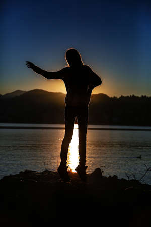 A vertical silhouette shot of a female jumping near the sea with the beautiful sunset in the backgroundの写真素材