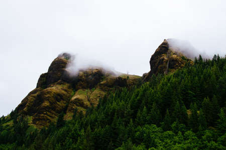 A scenery of smoke coming out of a mountain next to a forest full of green trees