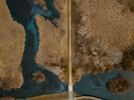 An aerial shot of a road in the middle of a dry grassy field with trees and riversの写真素材