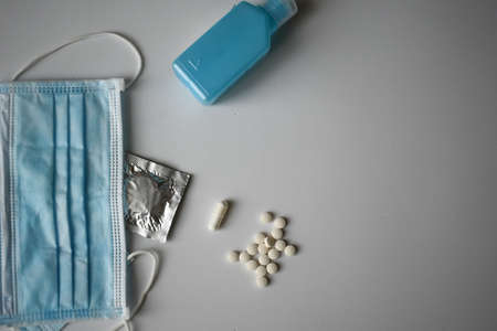An overhead shot of a medical face mask, medications, pills and a bottle of disinfectant on a white surfaceの写真素材