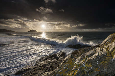 A beautiful shot of sea waves crashing on rocky cliffs under a sunny sky. Great for computer desktop wallpaperの写真素材