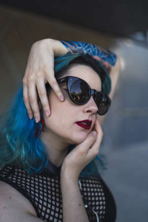 A portrait of a cool young lady with blue hair, tattoos, and sunglassesの写真素材