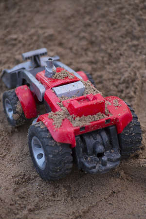 A vertical shot of a red plastic toy car in a sand box in a park