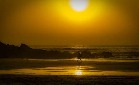 A male walking on the beach enjoying the beautiful view of the sunset reflected in the seaの写真素材