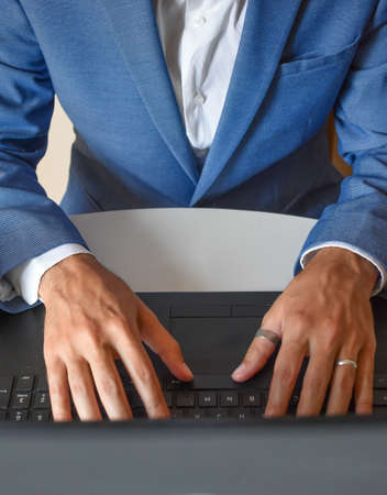 A selective focus shot of a young businessman in a blue tuxedo working on his laptopの写真素材