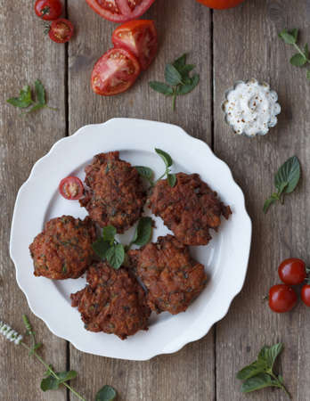 A high angle shot of cutlets in a white plate on a wooden surface with mint leaves and tomatoes on...