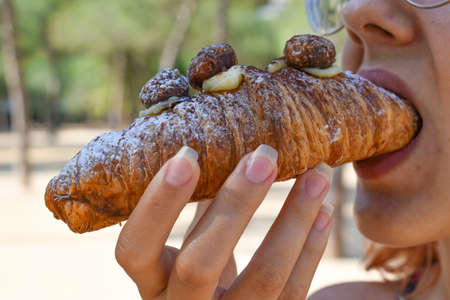 A closeup shot of a person eating a croissant at daytimeの写真素材