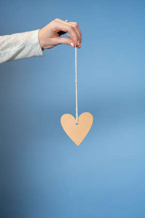 A vertical shot of a female holding a hearth shape attached to a rope with a blue background