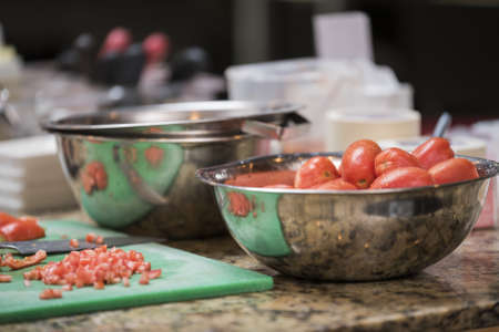 A bowl of tomatoes next to some bowls and kitchen appliancesの写真素材