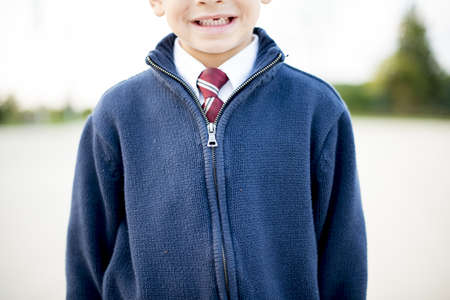 A closeup shot of a boy smiling in a white shirt with a tie under a blue jacketの写真素材