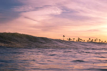 A horizontal shot of a body of water with waves during sunset with the purple sky above. Perfect for a wallpaper or a background.の写真素材