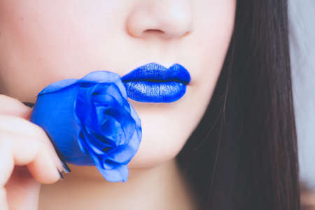 A closeup shot of a dark-haired female with a blue lipstick biting a blue rose - great for a fashion...