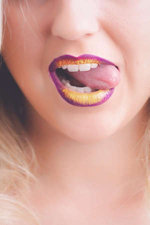 female with purple and yellow lipstick flirtatiously licking her lips.の写真素材