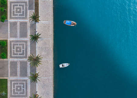 high angle shot of the stone shore with palms of the pure blue sea with two small boats in it