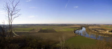 A wide shot of grassy fields near a river under a blue skyの写真素材