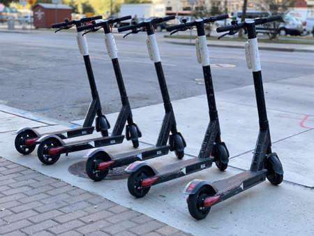 Five scooters parked on the sidewalk by a streetの写真素材