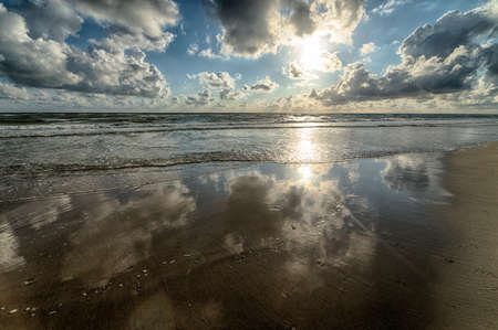 A breathtaking shot of reflection of the sunlight and the cloudy sky in the ocean next to the shore