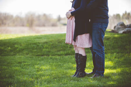 A closeup shot of a pregnant couple standing on a grassy field with a blurred backgroundの写真素材