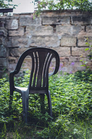 A vertical shot of a plastic chair on a grass covered field with a stone wall in a backgroundの写真素材