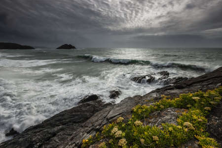 A beautiful shot of a water stream flowing near rocky cliffs with grass under a gray sky