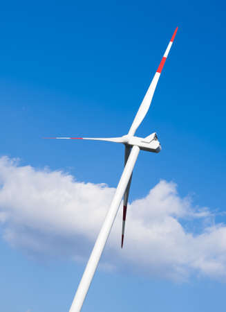 The modern, metallic and white wind turbine in the blu sky
