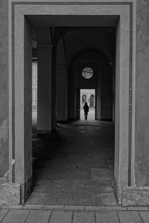 A vertical grayscale shot of a square arch and a silhouette of a person in the background - alone conceptの写真素材