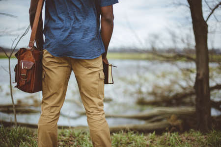 A closeup shot from behind of a male wearing a leather bag and holding the bible with a blurred...