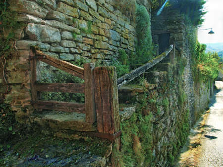 A horizontal shot of old stone stairs covered in moss with wooden gate and handrail in Rupit, Spain