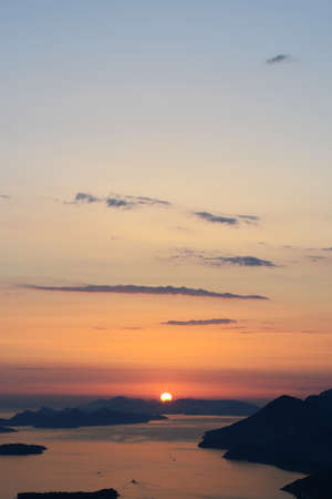 A vertical shot of the horizon with water and the sun setting in a breathtaking blue sky in the...