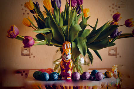 A closeup shot of bunny chocolate near easter eggs and flowers with a blurred background